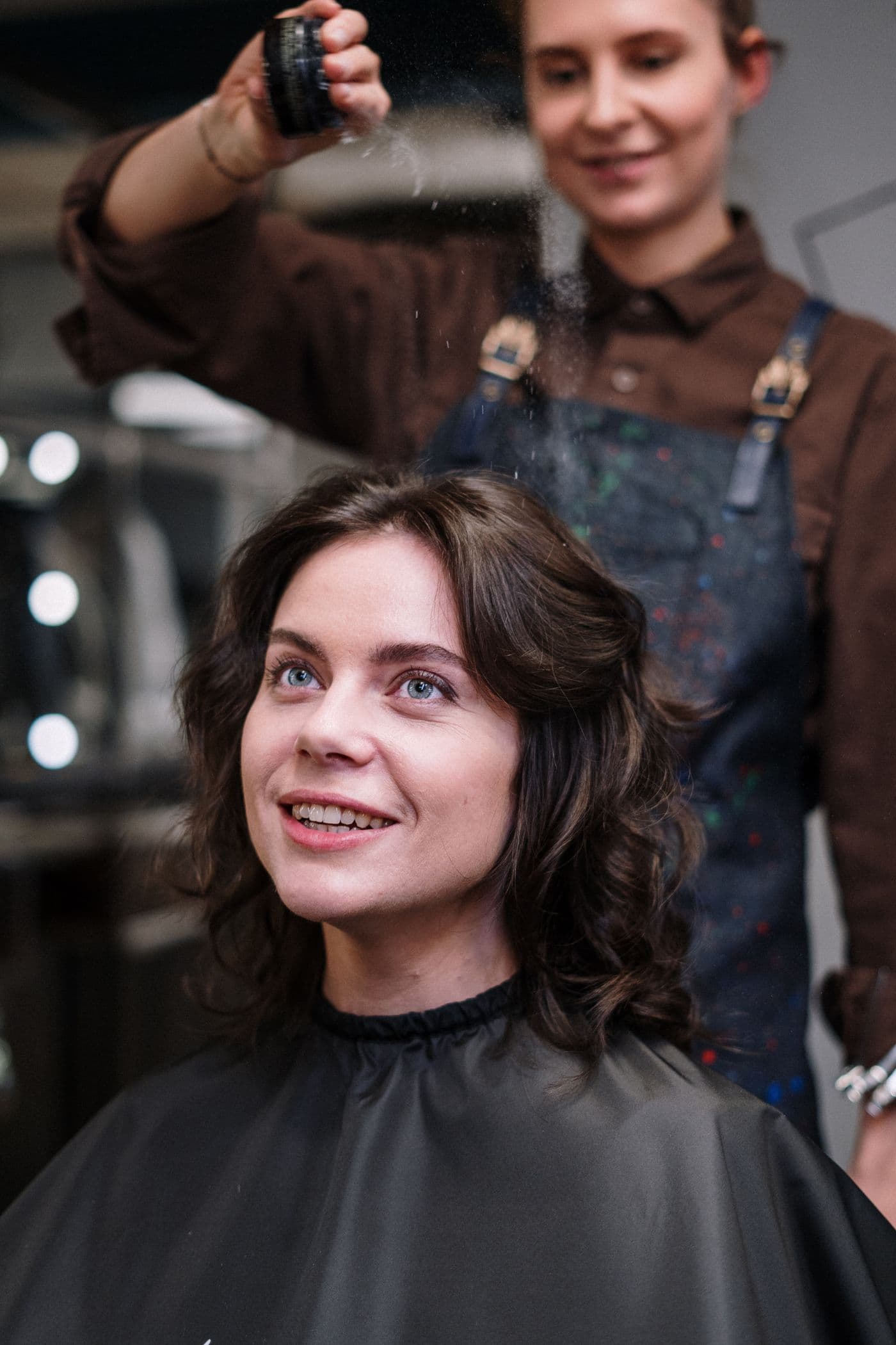 Cliente sorrindo na cadeira do salão enquanto a profissional trabalha atrás dela